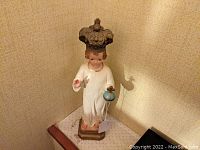 Full view of the statue showing the crowned child in a white robe standing on a base.