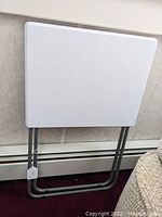 Side view of folded plastic top folding table against a wall.