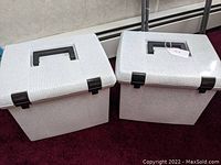 Two light gray speckled plastic file boxes with black handles and latches placed side by side on a carpeted floor.