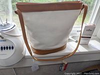 Large white leather handbag with tan leather trim and strap placed on a window ledge next to a blender and a carton of cream.