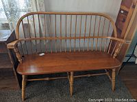 Front view of wooden Windsor style settee bench showing spindle back, armrests, and turned legs.