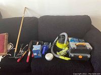 Photo of assorted garden hand tools, electric hand vacuum, boxed items, and toolboxes arranged on sofa