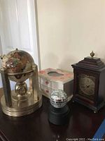 Photo showing four items: stone globe clock, jewelry box, miniature disco ball, and wooden desk clock on a white surface against a plain wall.