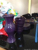 Overview of the purple ceramic dinnerware set and the tall matching vase arranged on a black surface.