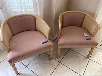 Pair of wooden barrel chairs with cane backs and pink upholstered seats and inner backs. Both chairs show stains on upholstery and scratches on wood frames.