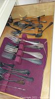 Flatware including forks and spoons loosely arranged in drawer with partially visible velvet holder
