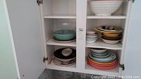 Dishware including large cream ceramic bowl, several medium and small bowls, and stacks of assorted plates in various colors.