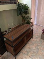 Entertainment console showing metal frame and wood-grain laminate shelves and edges, with some dust visible, placed against wall near electrical outlets.