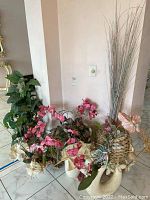 Five vases with mixed faux flowers including pink orchids, long grass-like stems, and green leafy plants placed on the floor.