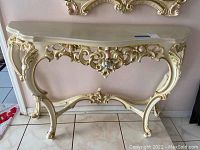 Full view of half moon console table showing cream color and ornate gold detailing on front and legs.