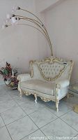 Front view of French Provincial style love seat with tufted back upholstery and ornate cream and gold wooden frame.