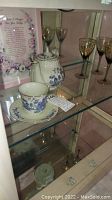 Porcelain Robinson Group teapot and matching cup and saucer with blue floral design along with three gold-decorated wine glasses in display cabinet.