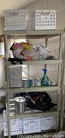 Full view of shelving unit with upper three shelves visible, holding plastic crates, cleaning spray, paints, ice bucket, shoes, and miscellaneous hardware items in bags.