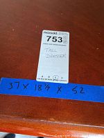Photo of a blue tape with dresser measurements handwritten 37 x 18.5 x 52 inches on the dresser surface.