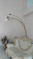 Full view of the gold tone arch floor lamp next to a vintage upholstered sofa and floral arrangement, showing the five curved arms and pink tulip glass shades.