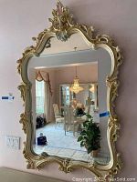 Full view of the wall mirror hung on a wall, reflecting a dining area with chandelier and chairs.
