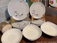 Most items neatly stacked on a wood surface showing dinner plates, salad plates and bowls with Frost Pine floral decoration.