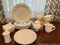 Wide angle of full ceramic set showing plates, bowls, teapot, creamers, cups, and incense burner all in cream color with lace and floral embossed patterns.