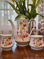 Front view of the three-piece tea set showing the teapot, sugar bowl and creamer with strawberry and flower design on porcelain.