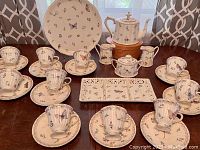 Complete set arranged on table showing all pieces including cups and saucers, coffee pot, serving trays, sugar bowl, and creamers, showcasing butterfly and floral pattern.