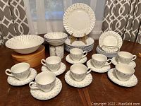 Photo of full 36-piece set including stacked plates, cups and saucers, and two bowl sizes displayed on table with patterned curtains background.