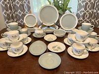 Full display of all 54 dinnerware pieces on table, showing plates, cups, saucers and creamer.
