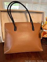 Full front view of brown leather handbag with black handles.