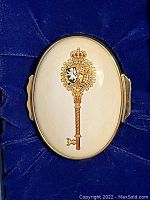Close-up photo of the oval enamel box showing the detailed Master Key design with royal crest and crown on cream background.