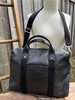 Front view of Jack Spade black leather briefcase tote with fabric vertical straps, dual handles, and crossbody strap.