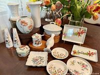 Photo shows entire collection arranged on table, includes various pieces of fine china such as trays, dishes, vase, salt and pepper shakers, lidded jar, porcelain figurine, and casserole dish.