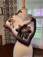 Silk scarf with floral design draped on a wooden mannequin showing detailed pattern and colors