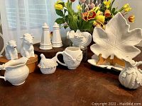 Overall view of assorted white ceramic and pottery items arranged on table, including animal figurines, various small vessels, leaf-shaped plates, and decorative pieces.