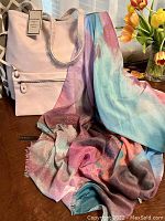 Photo of the GH Bass & Co. light pink reversible tote bag with removable pouch and the Love & Lore colorful silky scarf/wrap spread on a wooden table with flowers in the background