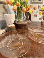 Photo showing six translucent pink etched glass salad plates arranged on a wooden table with floral motifs around the rim.