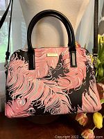 Front view of pink fern patterned handbag with black vinyl exterior and short black handles