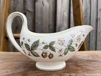 Side view of the Wedgwood Strawberry Hill gravy boat showing strawberry and flower detail with gold trim on handle and rim.