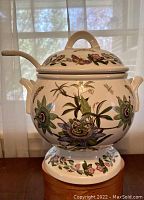 Full view of the closed soup tureen with lid and ladle inserted, showing botanical and butterfly designs
