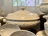 Large covered tureen with applied grape-vine relief around body and lid, flanked by scroll handles