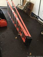 Full-length view of ladder lying on ground showing orange side rails and aluminum rungs