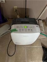Full frontal view of the dehumidifier showing power cord, vents, and handle on tiled floor.
