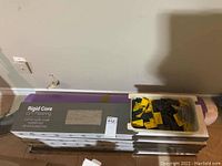 Stack of five Rigid Core LVT Flooring boxes with tub of yellow spacers on top, purple underlay visible