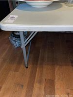 Close-up of table corner showing resin top edge and metal legs with rubber feet on wood flooring.