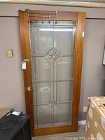 Full view of the wooden French door leaning against wall showing frame, glass insert, handle, hinges, and rack
