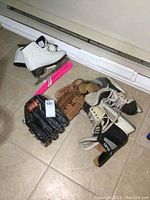 Photo showing the men's hockey skates, women's figure skates with pink blade guards, and two left-hand leather ball gloves on the floor.