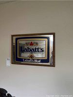 Front view of Labatt's Blue clock sign mounted on wall, showing mirrored background, blue and gold design, and wooden frame.