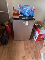 Front view of mini bar fridge showing stainless steel door with items on top and surrounding boxes.