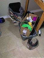 View of duffle bag with painting brushes and tools, paint rollers, and several paint cans on floor.
