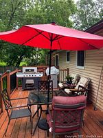 Overall deck view showing square glass-top table with red umbrella, four metal chairs