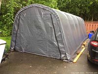 Three-quarter view of assembled portable garage showing front end panel with closed zipper door and arched roof structure