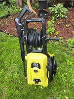 Front view of yellow/black pressure washer unit with hose reel and attached cord
